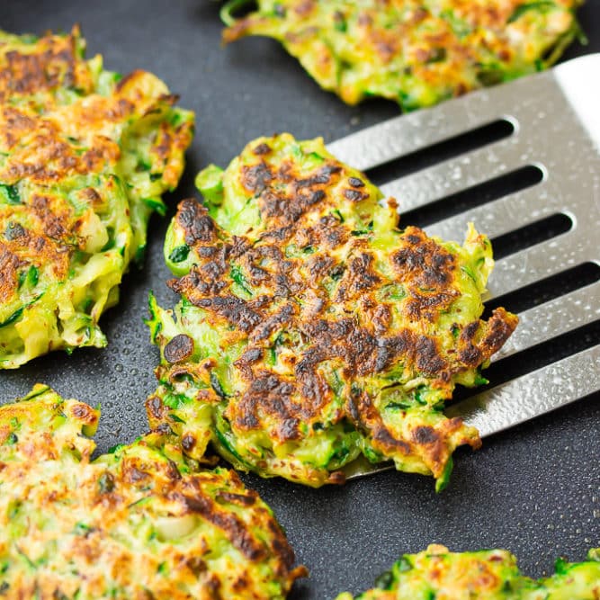 square image of a pan with fritters, one being lifted out with a spatula