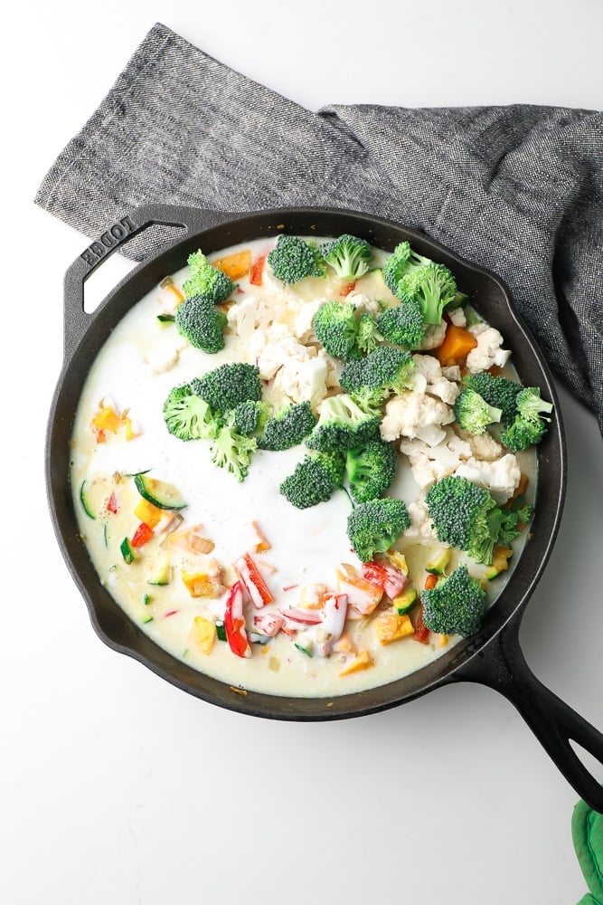 pan full of vegetables and coconut milk, fresh broccoli on top