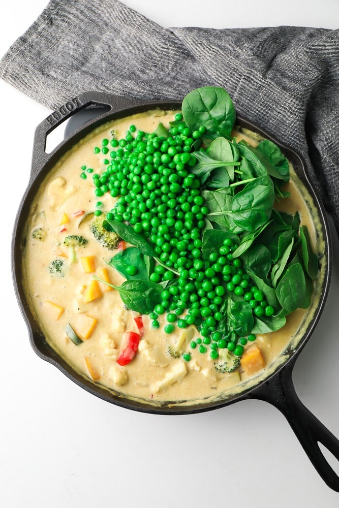 creamy sauce with vegetables in a pan with peas and spinach