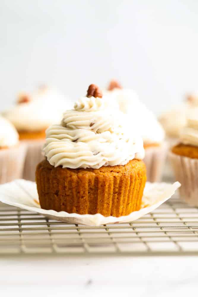 an orange cupcake with frosting, more in background, pecan on top