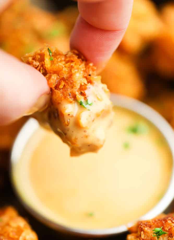piece of crispy vegan chicken nugget being dipped in yellow sauce