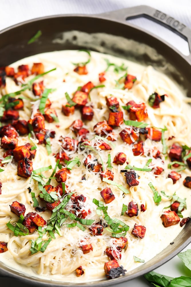 creamy vegan carbonara with tofu chunks and basil in black pan