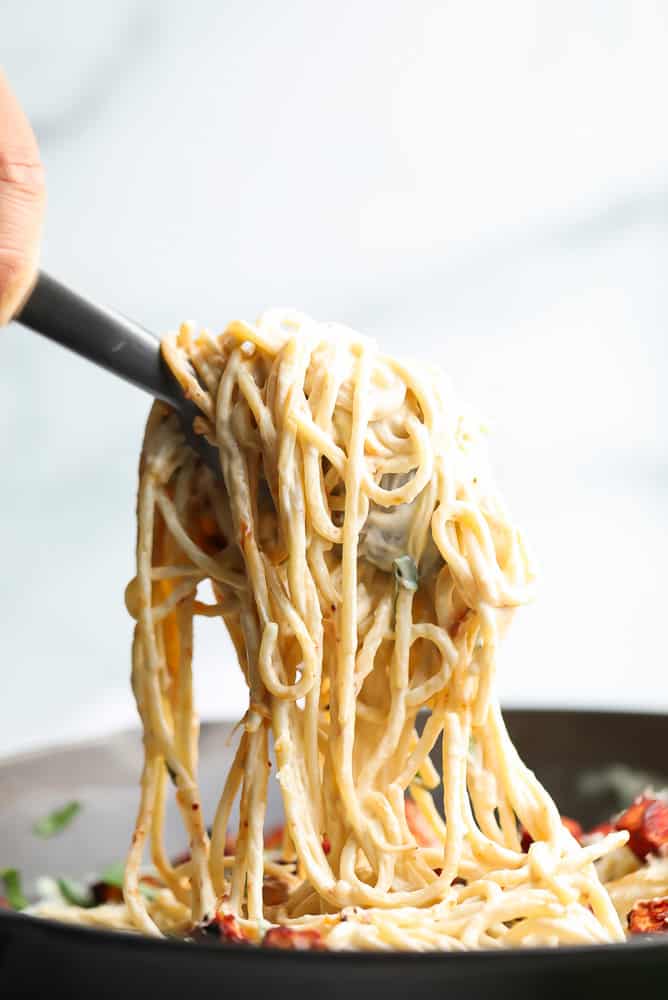 tongs holding a bunch of vegan carbonara spaghetti noodles