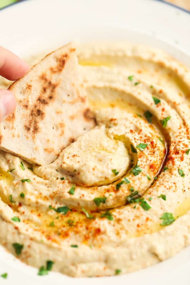 pita bread being dipped into a bowl of hummus