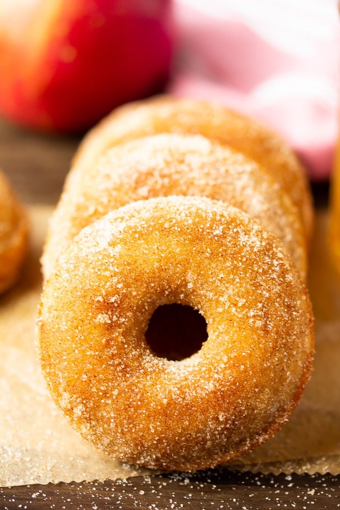 horizontal stack of sugar glazed donuts, apples in background