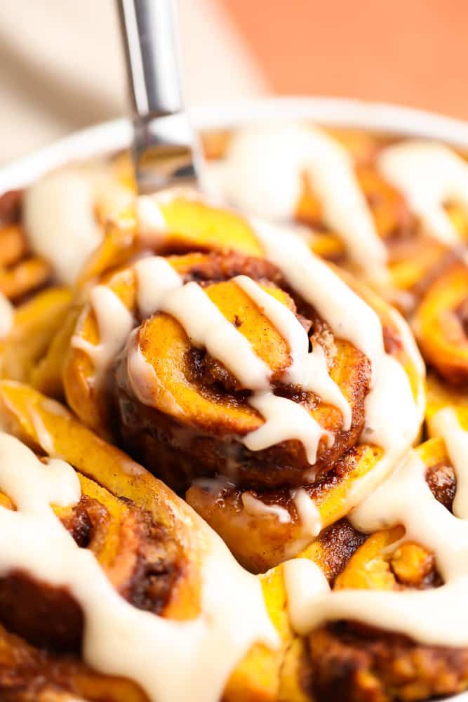 a pumpkin cinnamon roll being lifted out of a dish