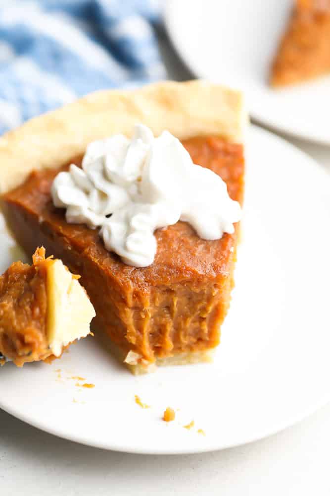 a fork taken out of a piece of sweet potato pie with whip cream on top