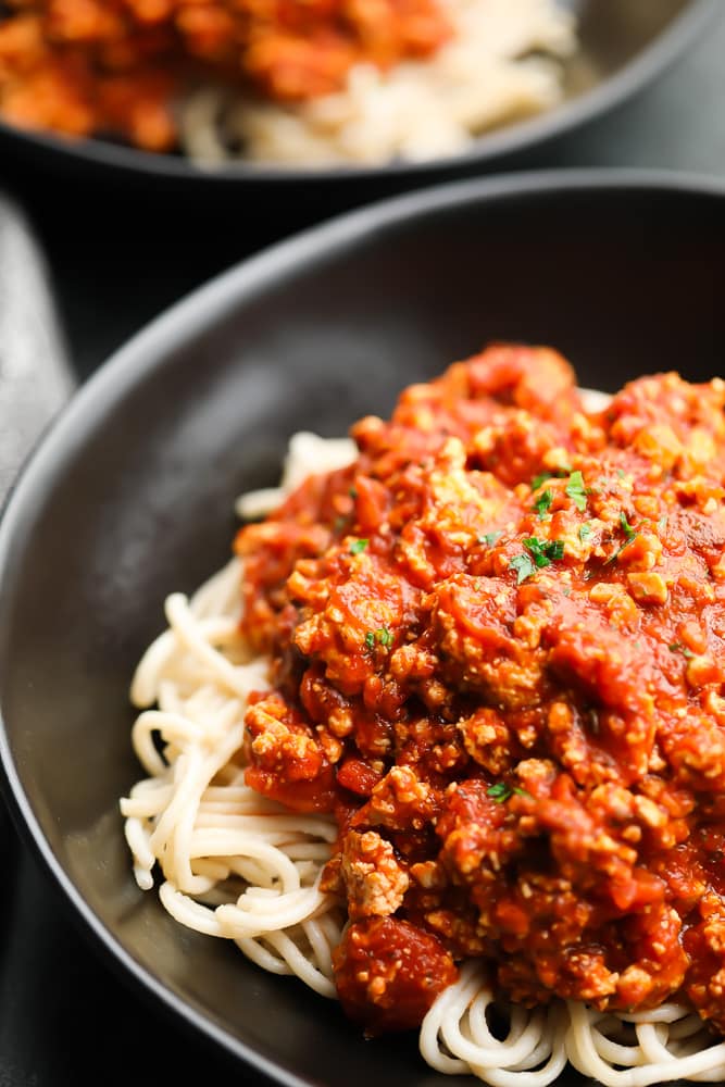 close up of vegan bolognese sauce in black bowl over pasta