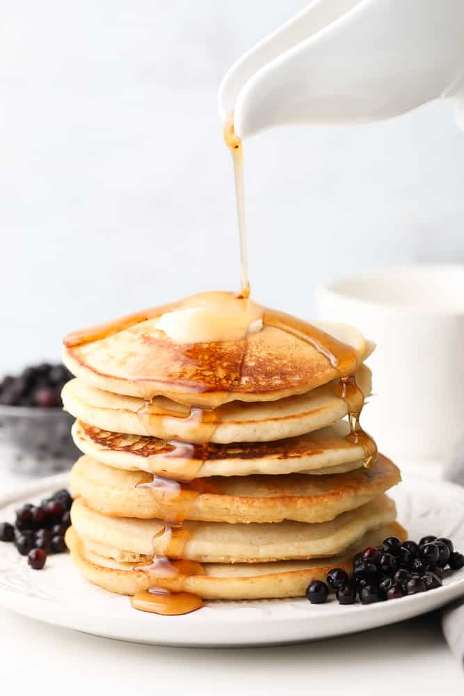 syrup being poured onto a stack of golden pancakes