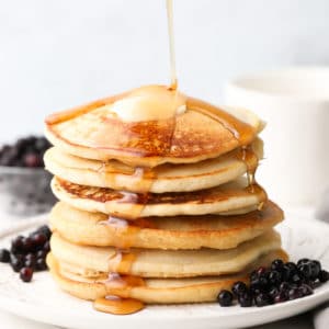 square image of pancake stack with syrup being poured, blueberries around them