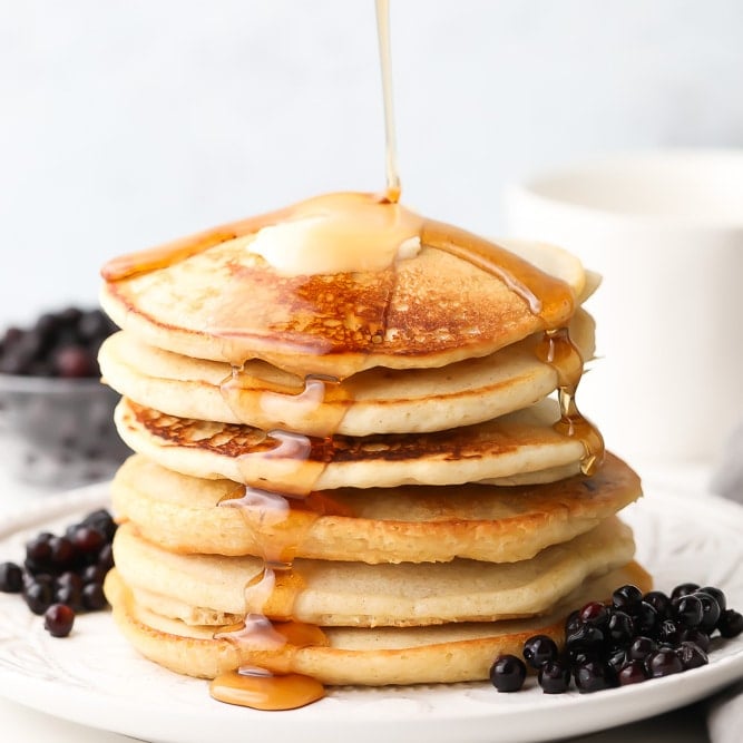 square image of pancake stack with syrup being poured, blueberries around them