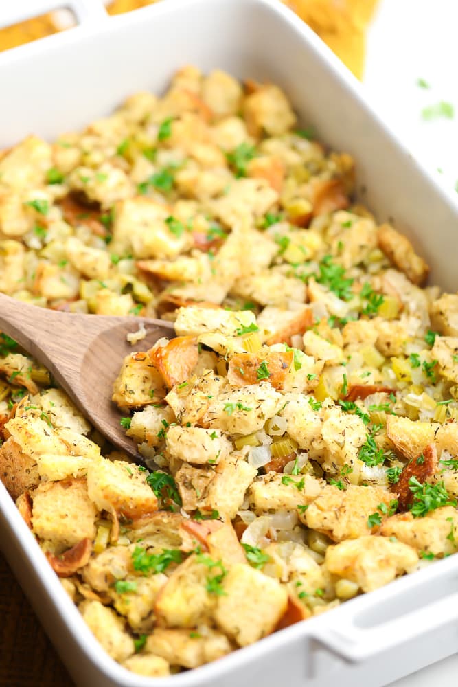 close up on a wooden spoon scooping up vegan stuffing from a casserole dish.