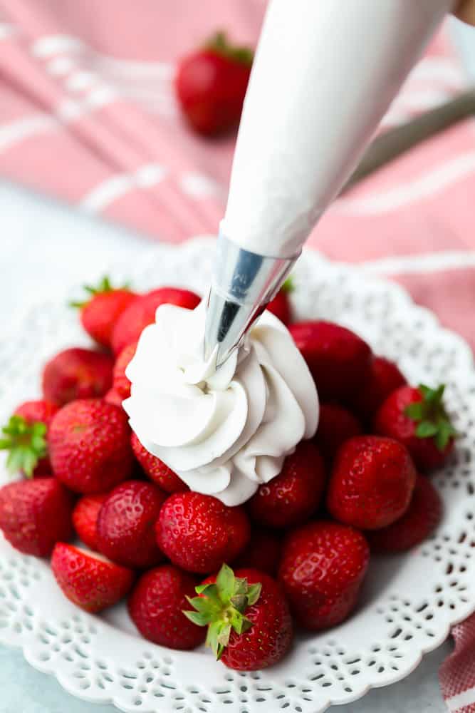 piping whipped cream onto some strawberries