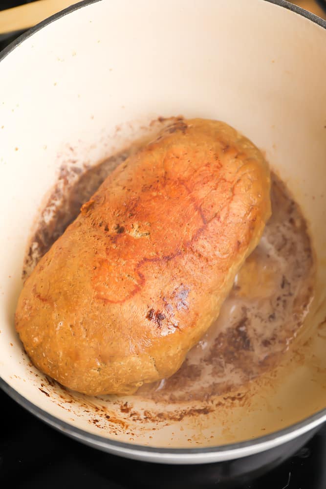 a vegan turkey loaf being browned in a white pot with butter