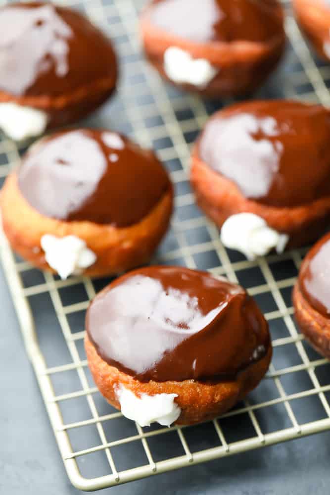 lots of cream filled chocolate topped donuts on rack