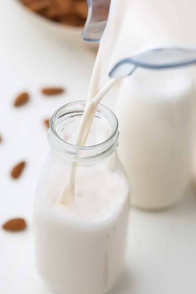 milk pouring into glass bottle from blender