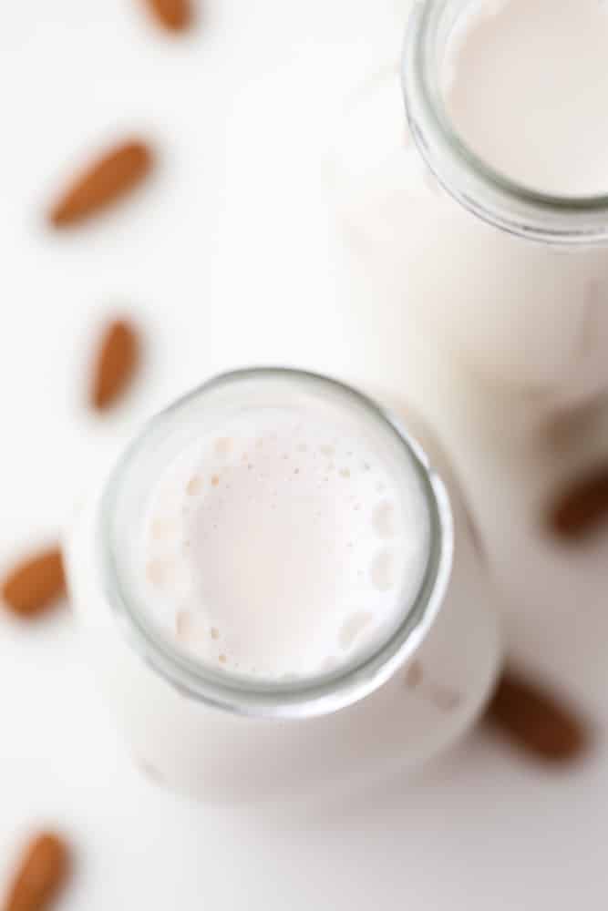 looking down on a bottle with white milk, almonds in background