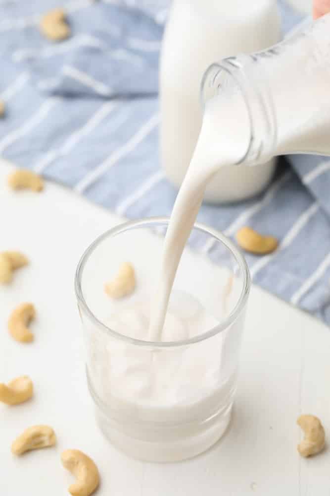 white milk with cashews in background being poured into cup