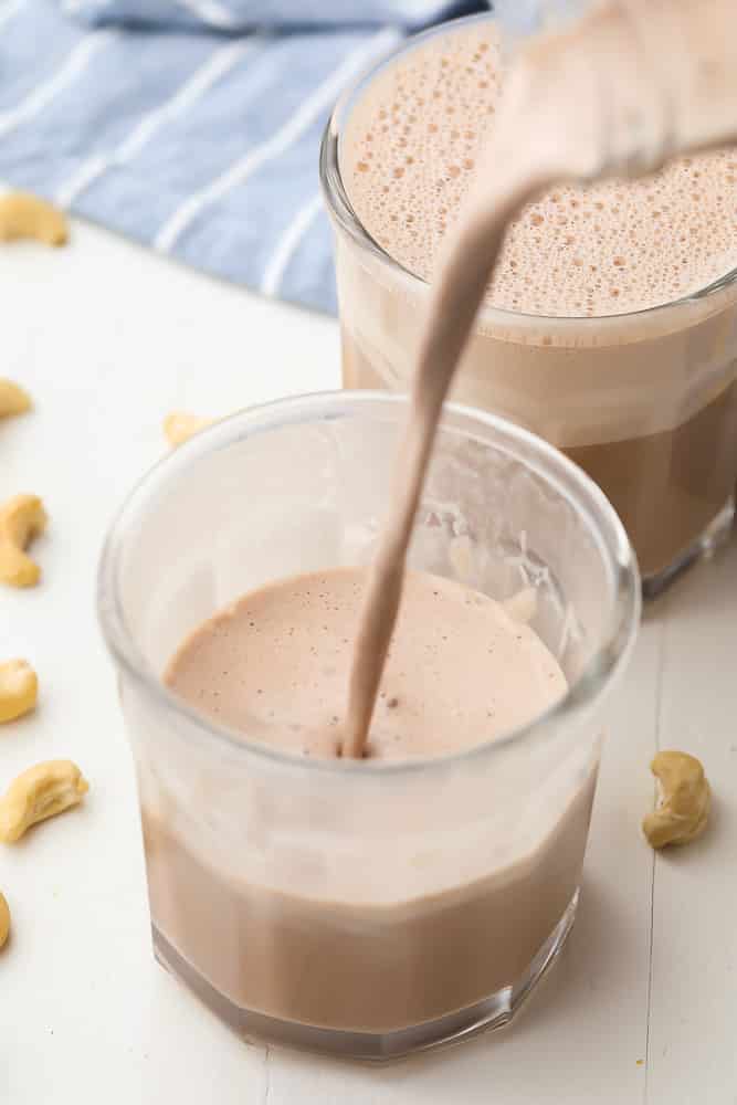 chocolate cashew milk being poured into a cup from a jar