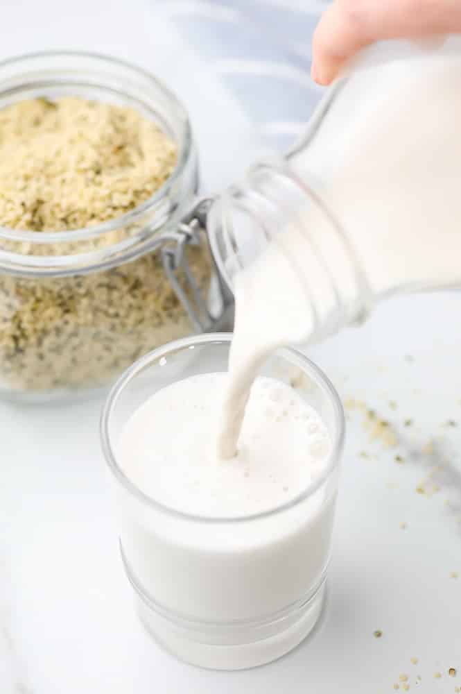 milk pouring in a cup from a jar with hemp seeds in background