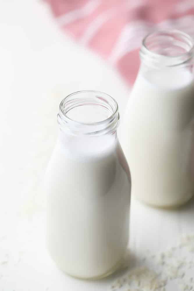 two bottles of creamy milk with coconut shreds all around