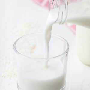 square image of a glass of milk being poured into a cup from jar
