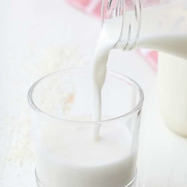 square image of a glass of milk being poured into a cup from jar