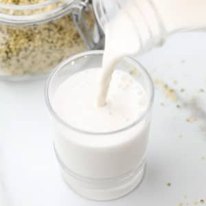 square image of milk pouring into a cup with hemp seeds in back