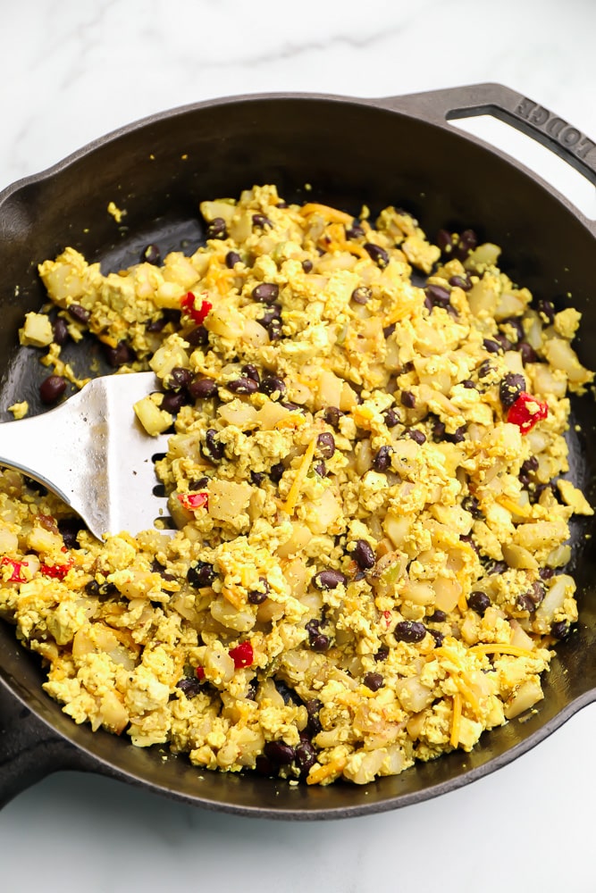 Frying tofu scramble, black beans, and potatoes in a cast iron pan