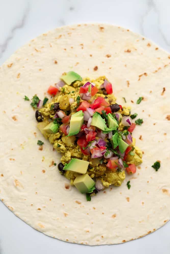 Tofu scramble, beans and potatoes on a tortilla topped with avocado and tomato