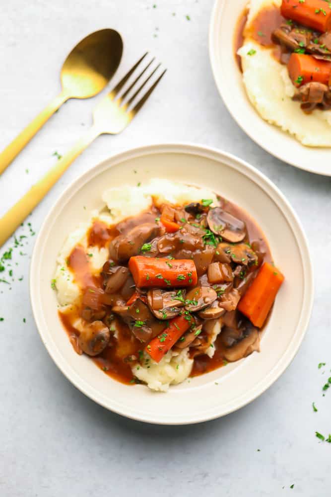 A white bowl with mashed potatoes and a vegetable stew on top