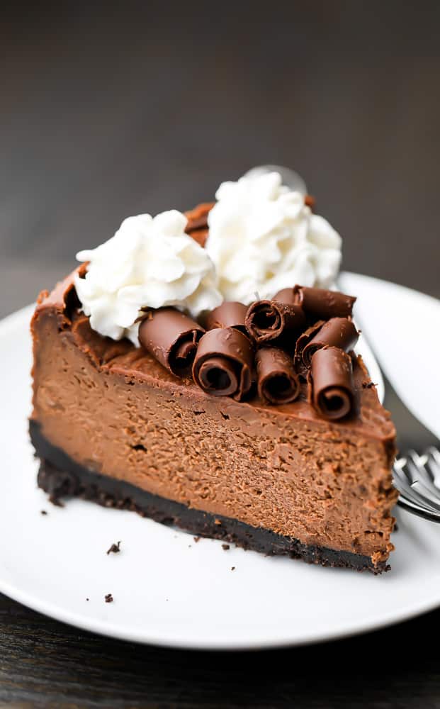 Slice of vegan chocolate cheesecake with whipped cream and chocolate on top on a white plate