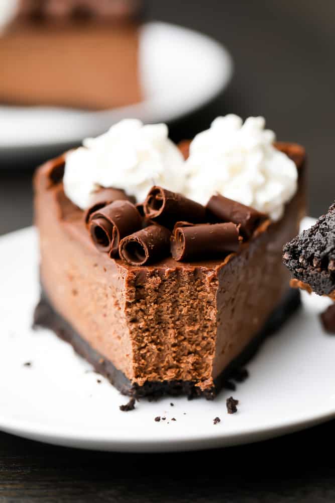 Close up of a slice of chocolate cheesecake on a white plate with a bite taken out of it