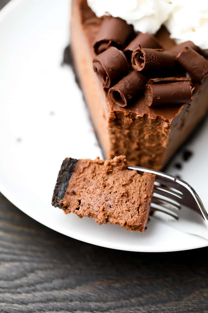 Fork taking a bite out of a slice of chocolate cheesecake on a white plate
