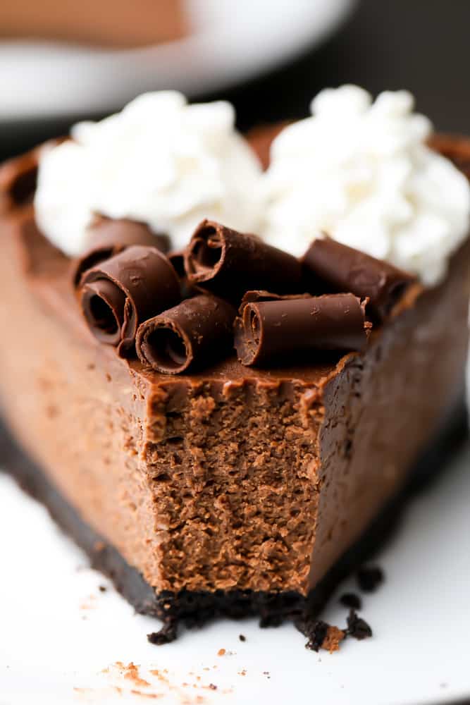 Close up of a slice of chocolate cheesecake on a white plate with a bite taken out of it