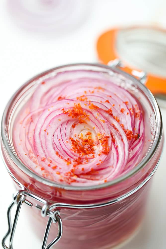 close up of sliced red onions in a mason jar with red flakes on top