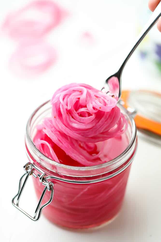 scooping pickled red onions out of a jar with a fork