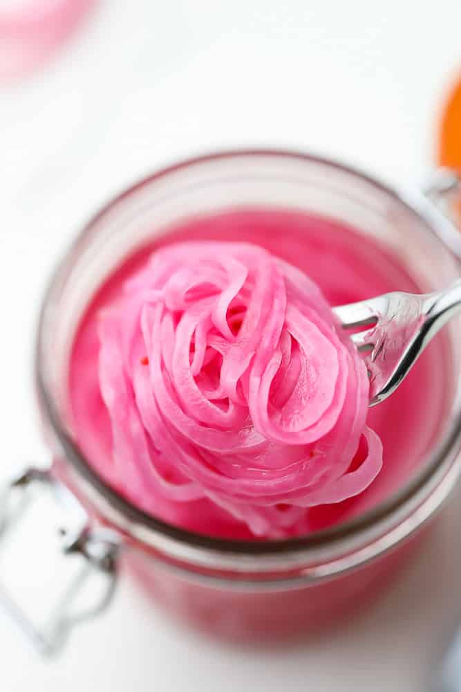 close up of a fork taking a scoop of pickled red onions out of a mason jar