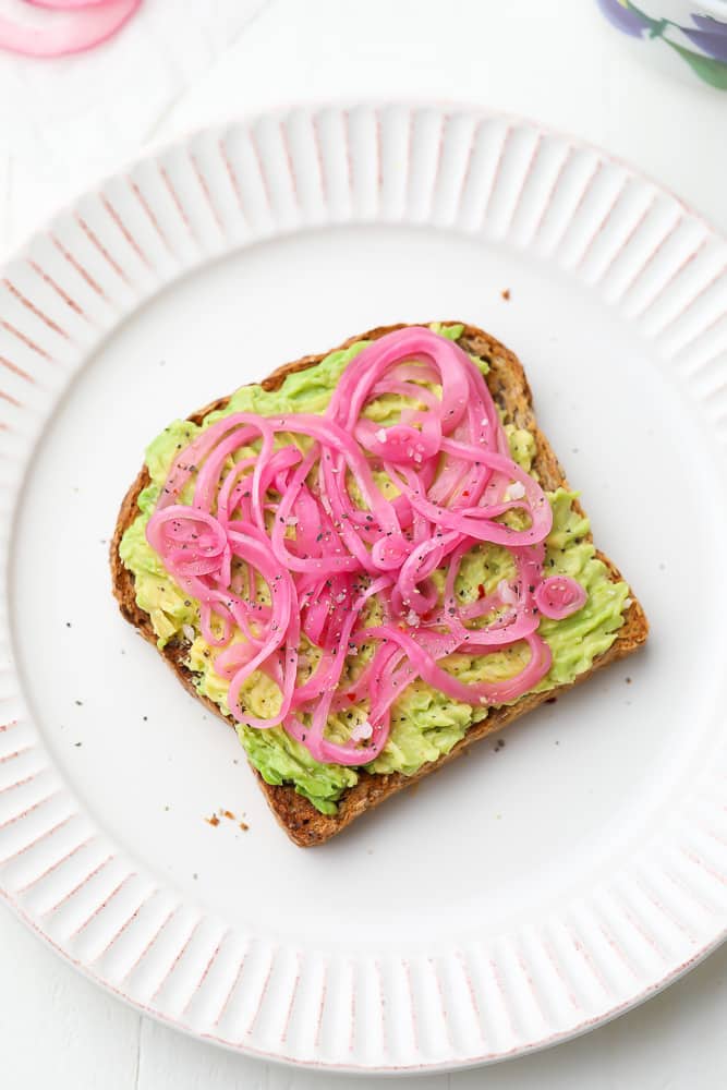 slices of pickled red onions on a piece of avocado toast on a white plate