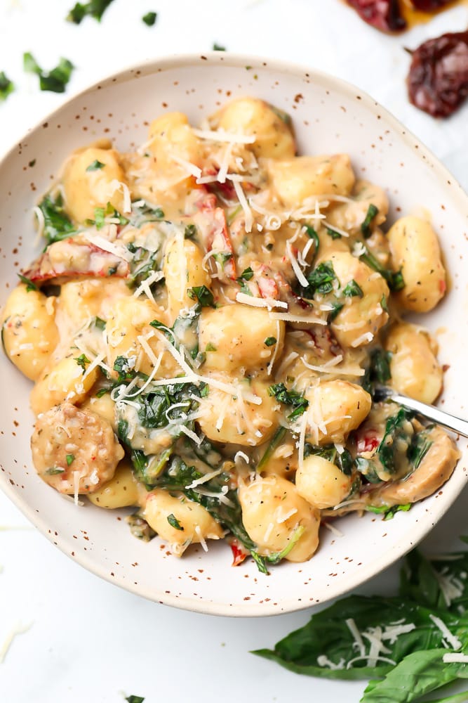bowl of vegan gnocchi with spinach and sun dried tomatoes in background