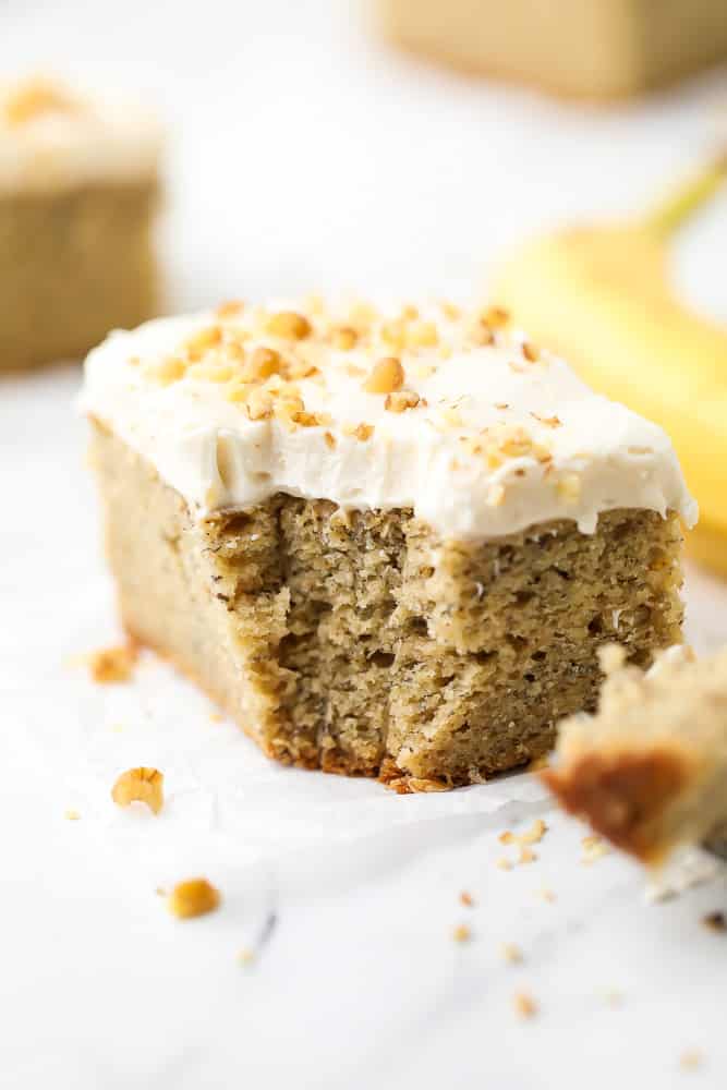 piece of cake with bite taken and walnuts and frosting on top with banana in background