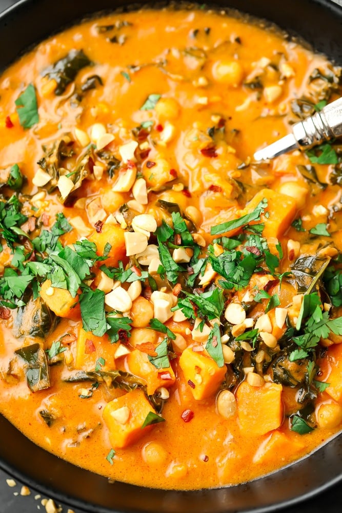 close up of a bowl of orange peanut soup with cilantro and peanuts on top