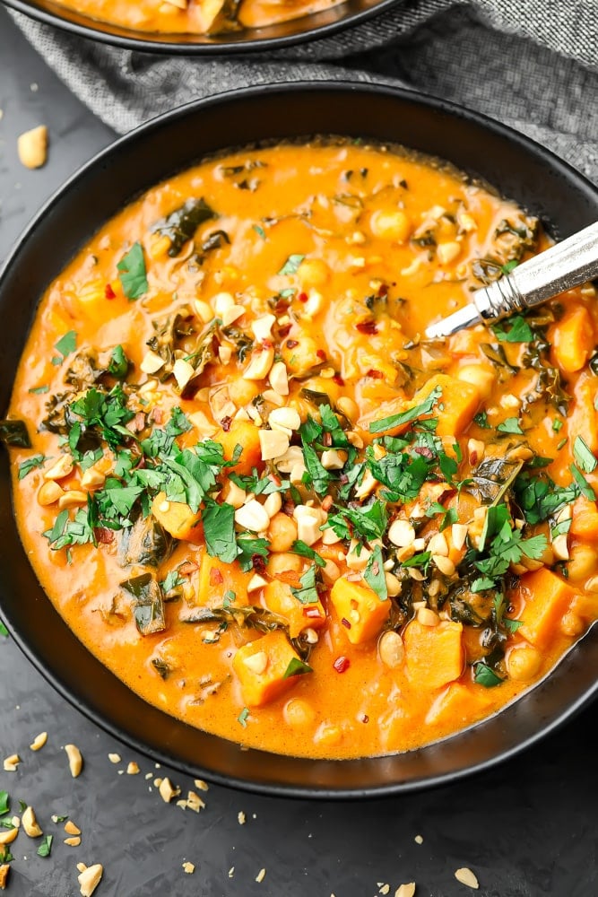 black bowl filled with orange peanut soup with cilantro and peanuts on top