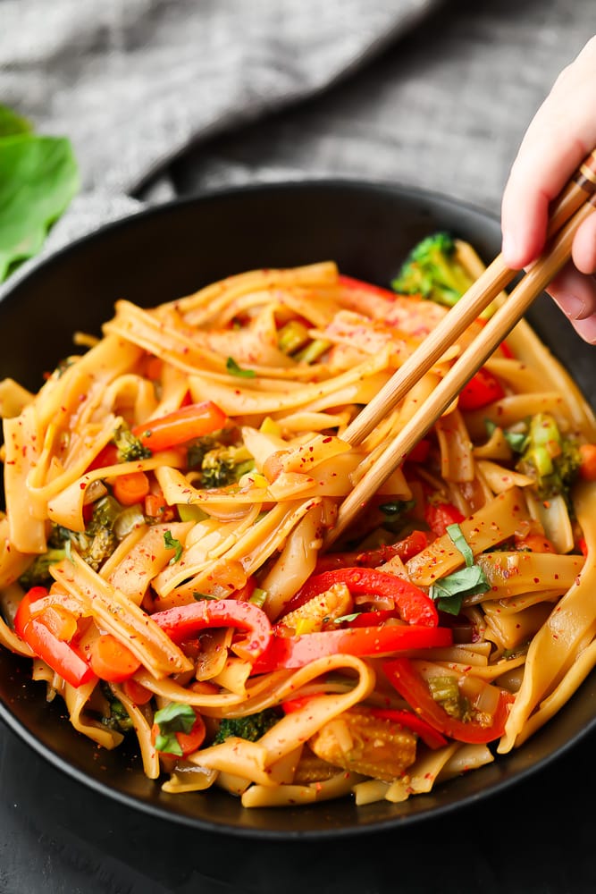 chopsticks holding some noodles out of black bowl