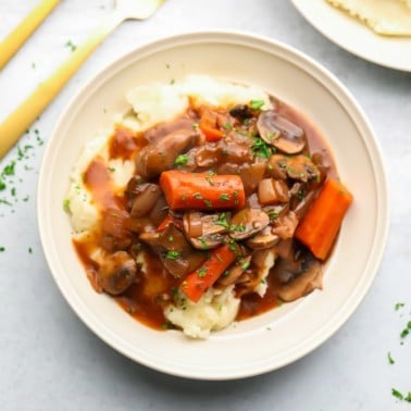 A white bowl with mashed potatoes and a vegetable stew on top