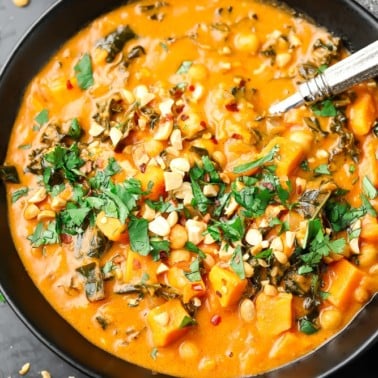 black bowl filled with orange peanut soup with cilantro and peanuts on top