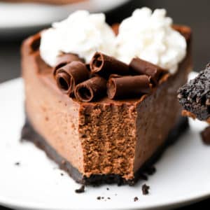 Close up of a slice of chocolate cheesecake on a white plate with a bite taken out of it