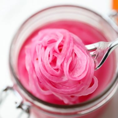 close up of a fork taking a scoop of pickled red onions out of a mason jar