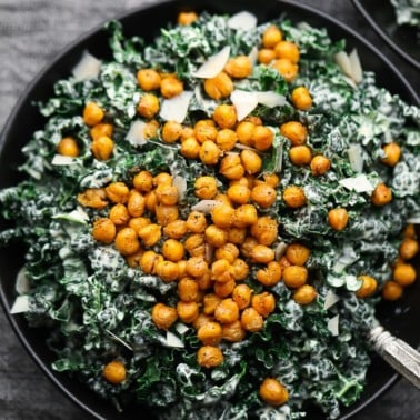 close up of kale caesar salad in a black bowl with chickpea croutons