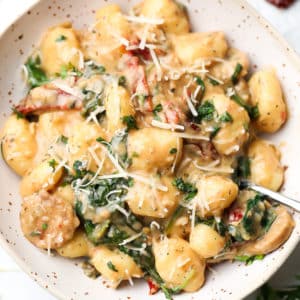 close up square image of pasta in bowl with spinach and tomatoes